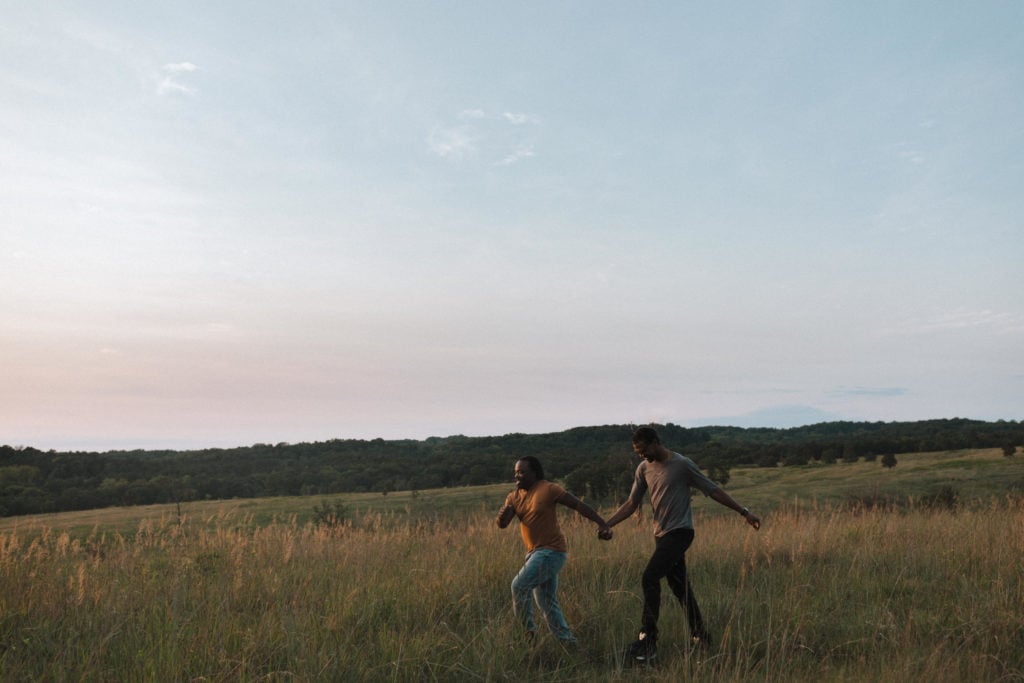 two men holding hands at sunset frolicking through a grassy meadow