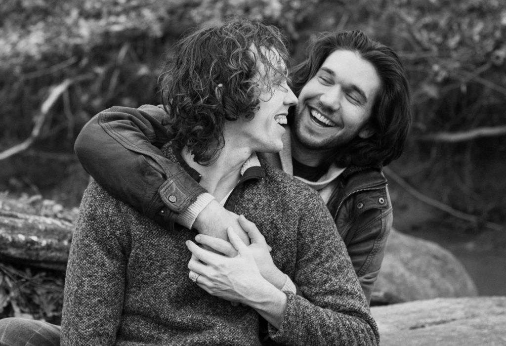 black and white photo of a man giving another man a hug from behind both laughing and in love