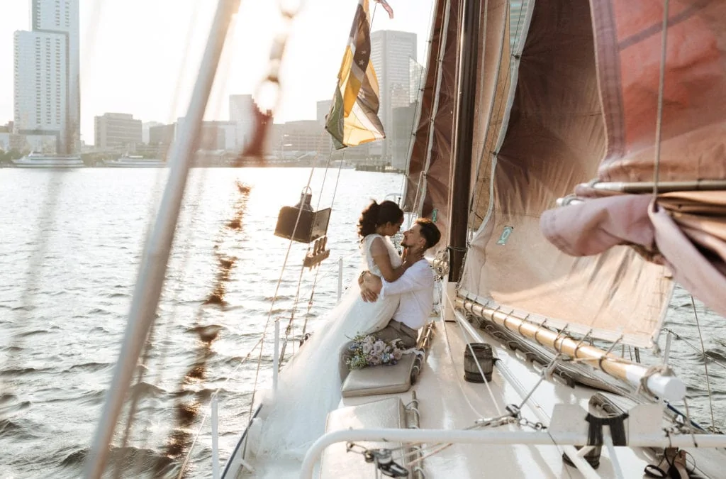 a bride and groom look lovingly into each other's eyes while on a sailboat during their elopement. the bride is in a long white wedding gown and the groom is in a white button up