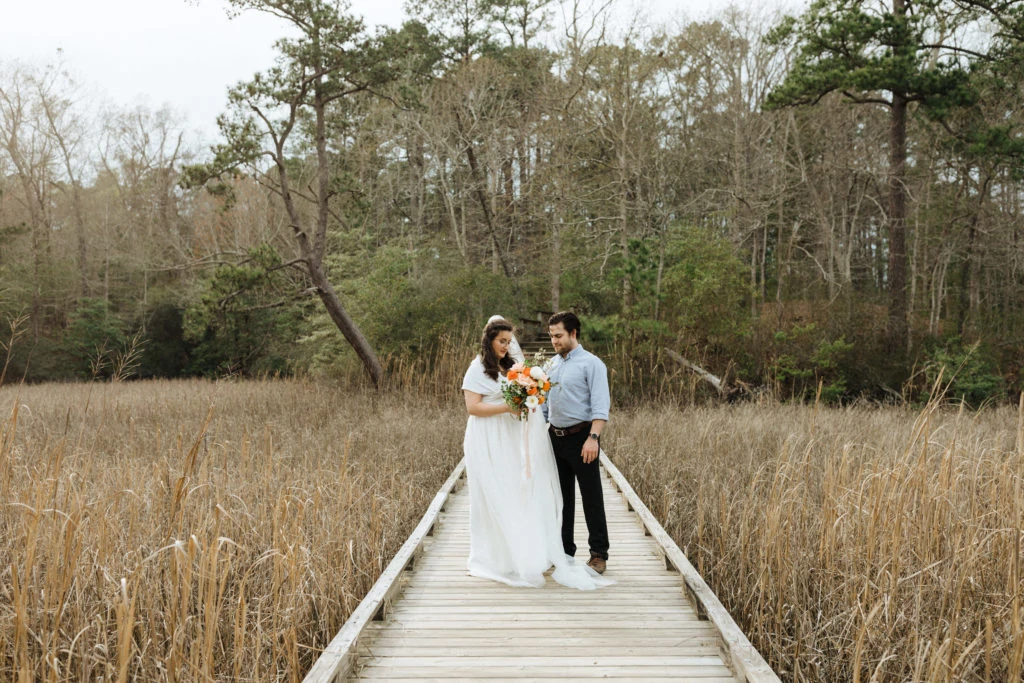 a bride in a wedding dress and the groom stand on the boardwalk on their way to fossil beach to get married at york river state park
