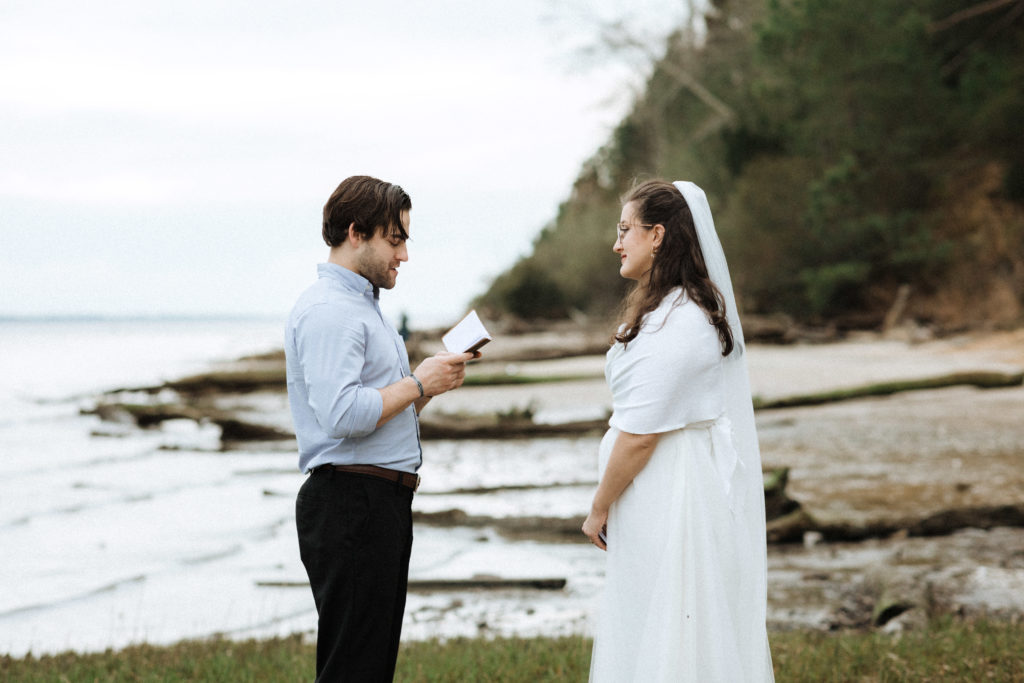 a groom reading his vows to his bride standing on fossil beach