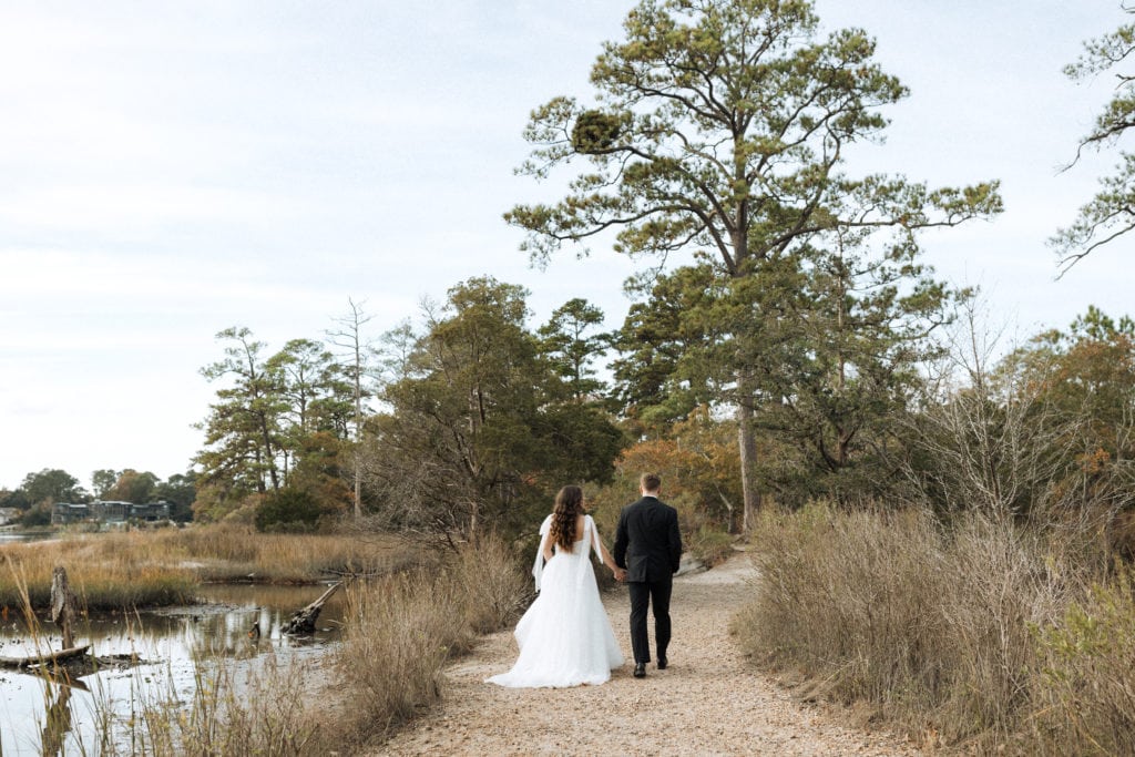 couple eloping in virginia holding hands walking through the marsh