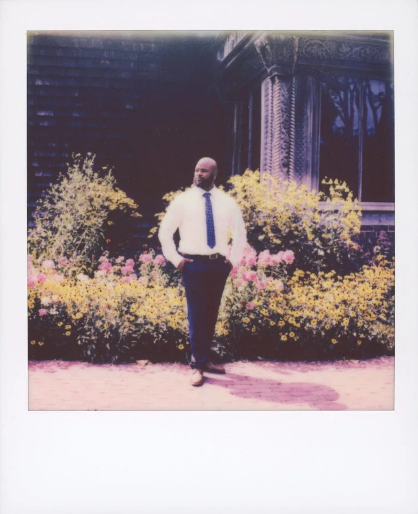 a polaroid photo of the groom in front of some beautiful yellow and pink flowers