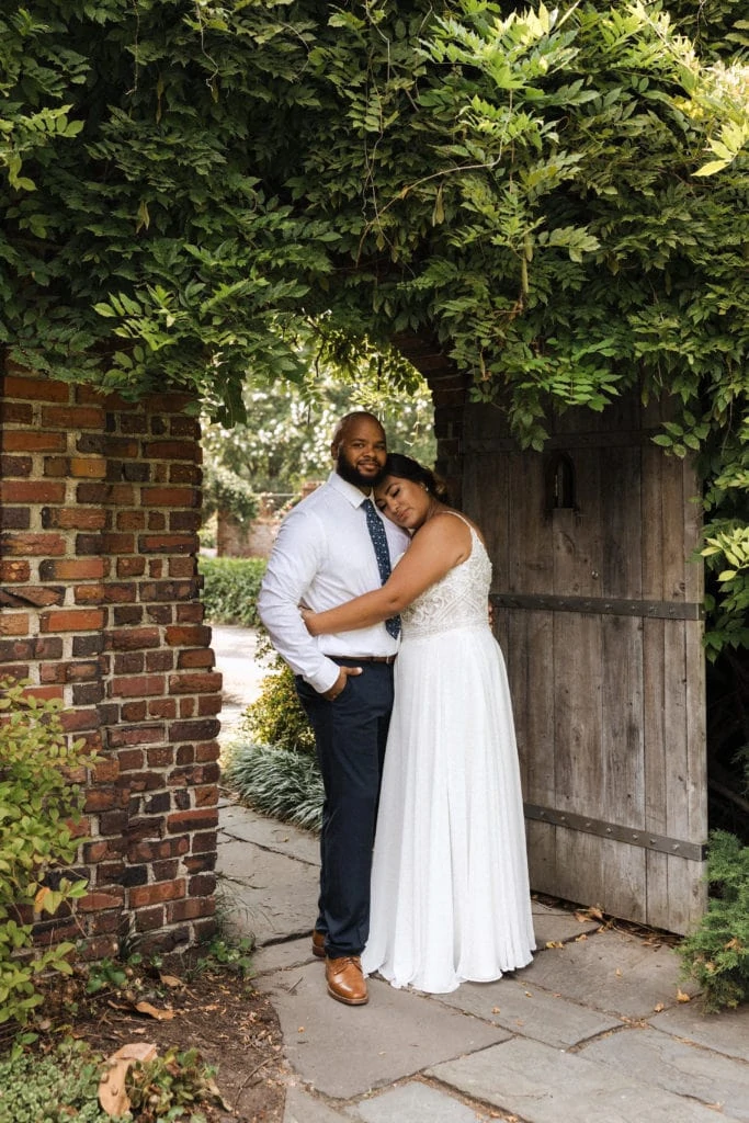 bride and groom hug in a brick archway with greenery around