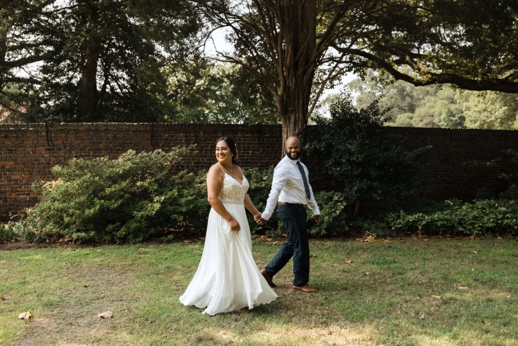 bride and groom holding hands as they walk in the garden smiling