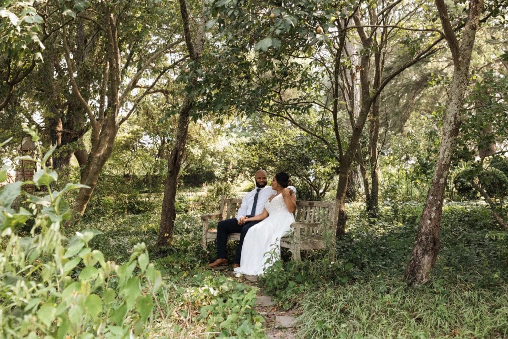 bride and groom sit on a bench in the forest