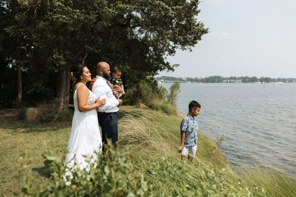 a bride and groom look out at the ocean with their infant and young son