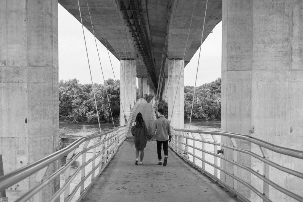 a couple holds hands walking under Richmond's Lee Bridge on the pedestrian suspension bridge on the way to Belle Isle