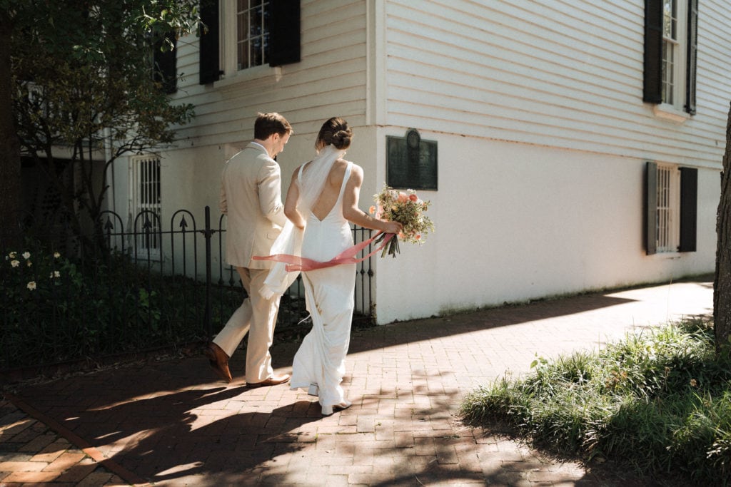 couple in wedding attire with bouquet walking on cobblestone streets in norfolk freemason district