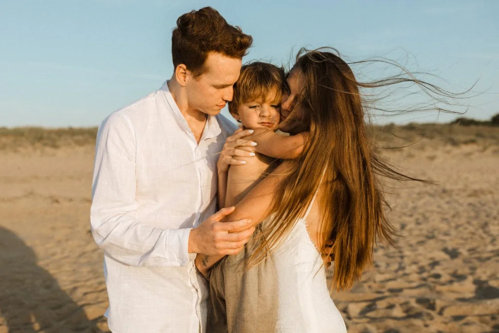 bride and groom hug their young son as golden light from sunset shines on them