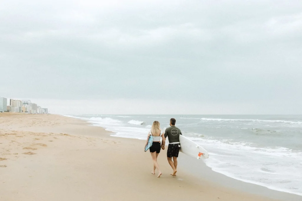 couple holding and and their surfboards in virginia beach on an overcast day walking away