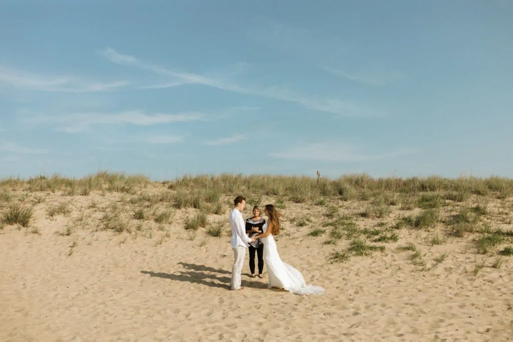 a couple having their wedding on the beach of first landing state park they are in wedding attire