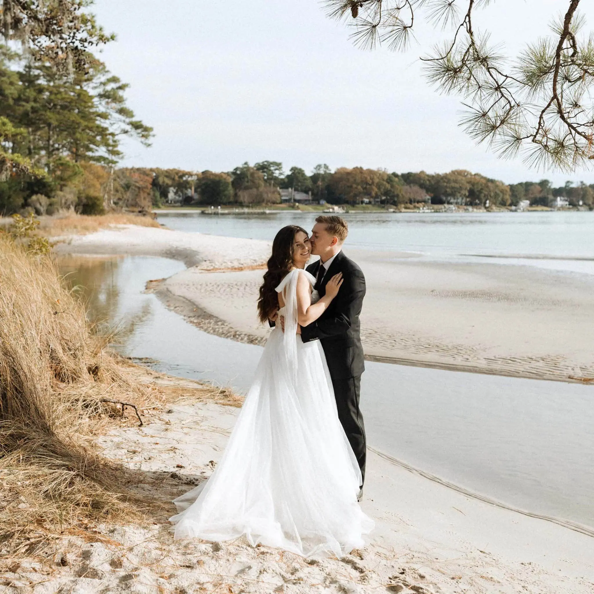a couple in wedding attire embrace by the water of first landing state park