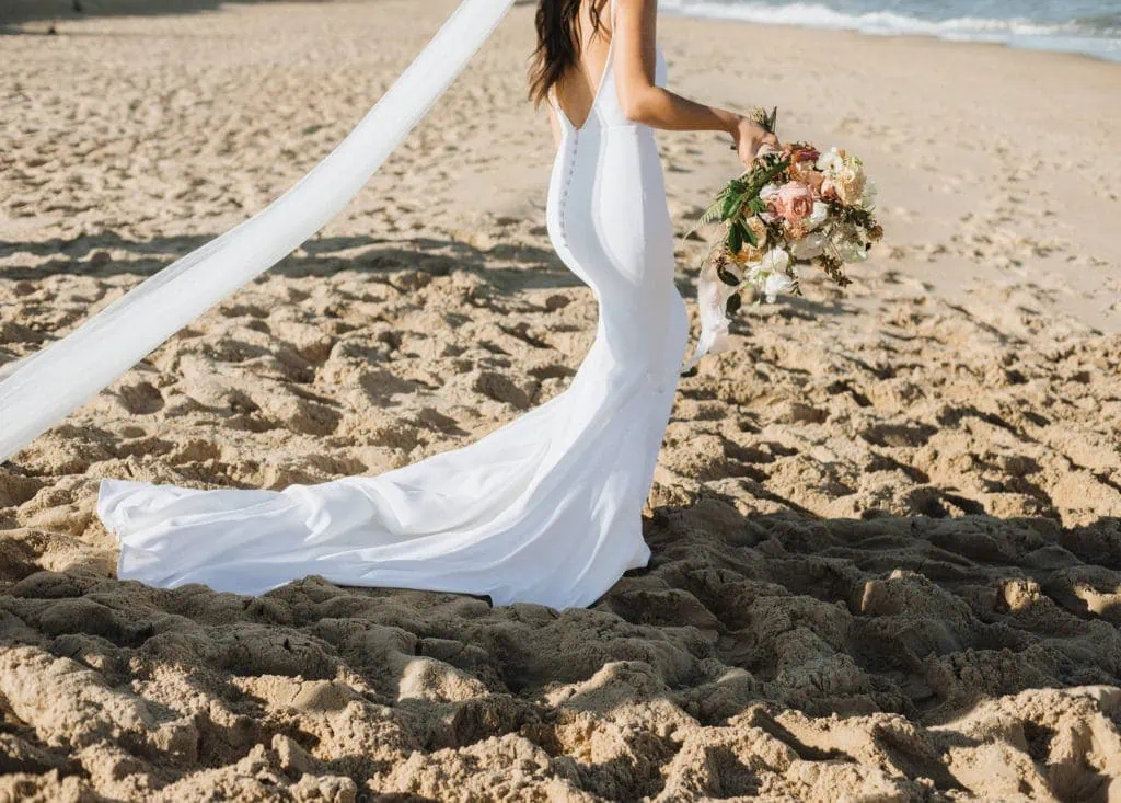 a bride on the beach holding a bouquet as she walks through the sand