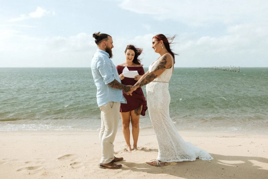 a couple say their vows on the beach with their officiant at first landing