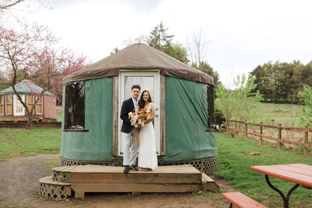 bride and groom standing in front of yurt at campsite in their wedding attire