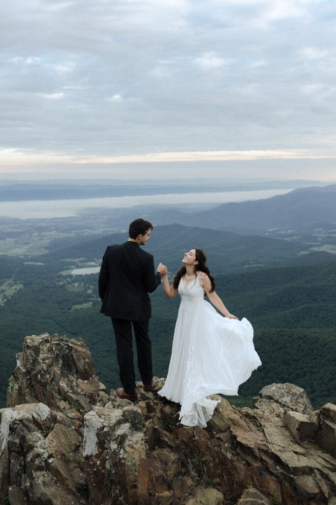 bride smiling at groom on a mountain with her dress flowing in the breeze