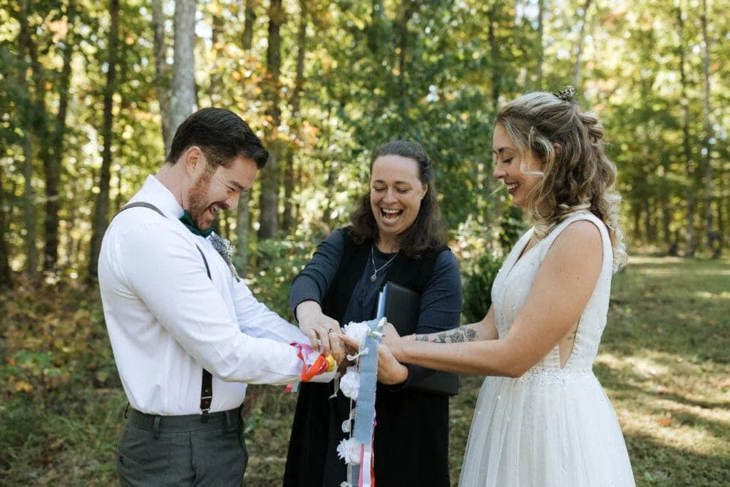 bride and groom laughing with officiant during wedding ceremony hand fasting