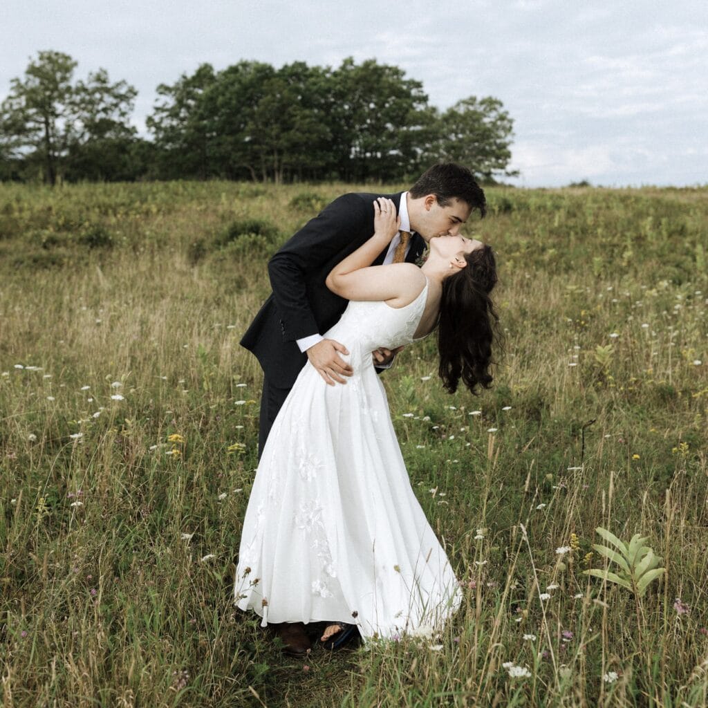 a groom dips his bride into a kiss in the middle of a wildflower meadows