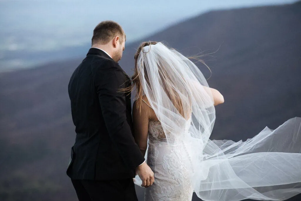 a bride and groom look out at the blue and purple mountains of the shenandoah valley
