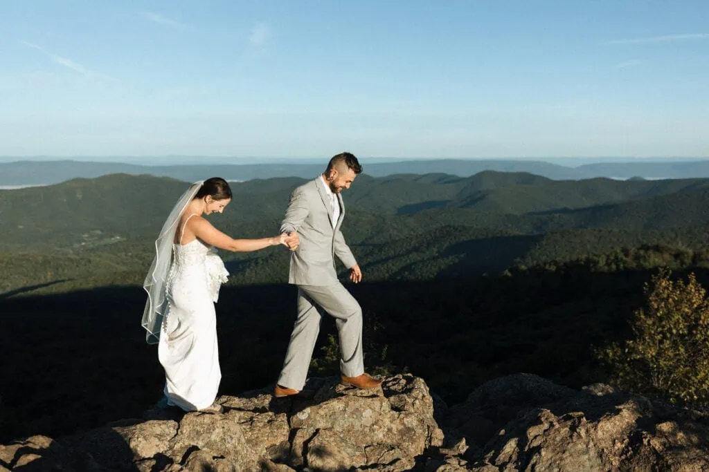 groom holding his bride's hand and leading her through the mountains