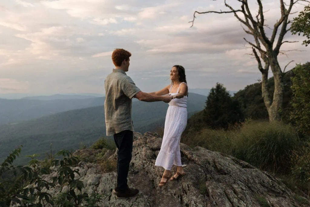 a couple holds hands and laughing at each other at sunset on Skyline Drive with the mountains in the background