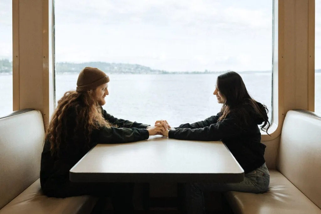 a couple sits inside the ferry and holds hands across the table smiling at each other