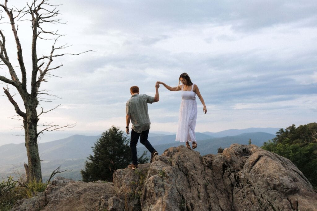 a man holding a woman's hand as they climb over rocks in the mountains. 